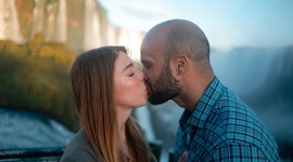 A photo of a couple sharing a kiss with waterfalls in the background